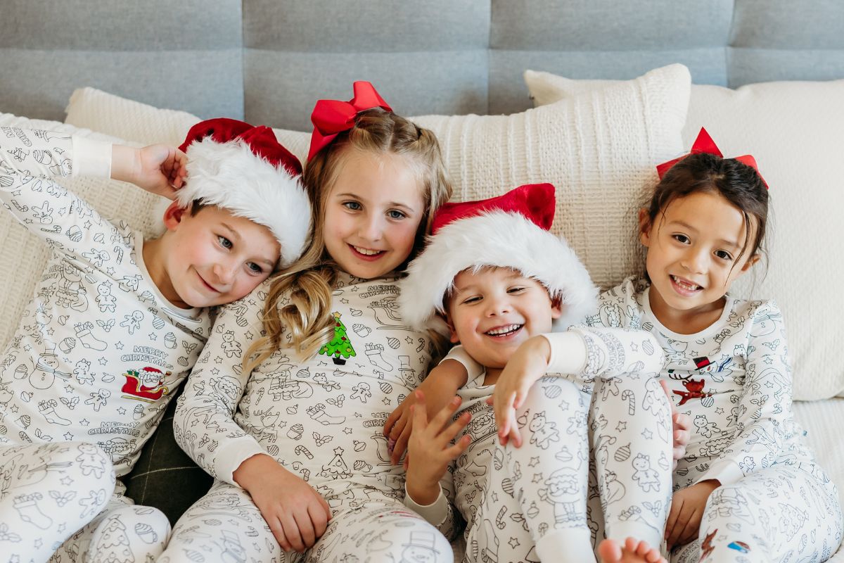 4 kids wearing coloring Christmas pajamas snuggled up on a bed. Bee Colorful Co.