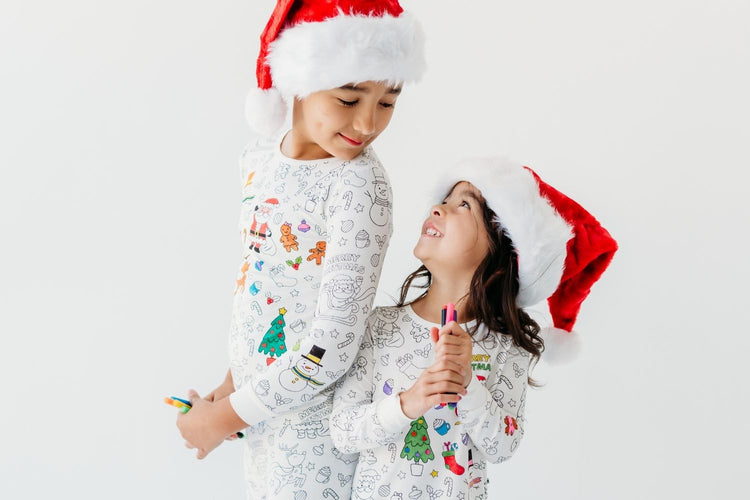 Siblings wearing Christmas coloring pajamas and holding fabric markers and smiling at each other