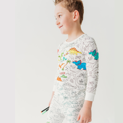 Boy wearing dinosaur bamboo coloring pajamas for kids holding fabric markers in hand